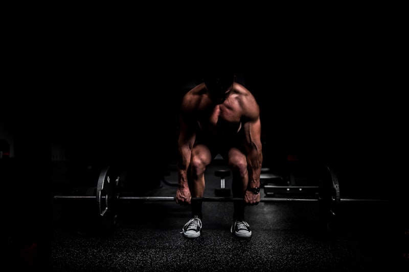 Person preparing to lift a barbell on the floor in a dimly lit gym